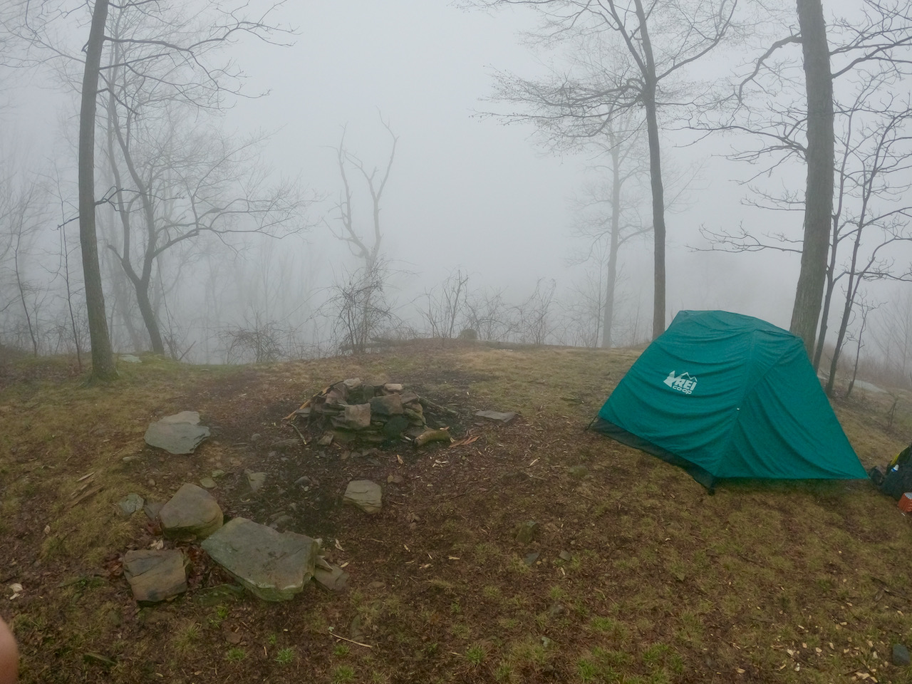 Photo of a primitive fire ring and tent surrounded by fog