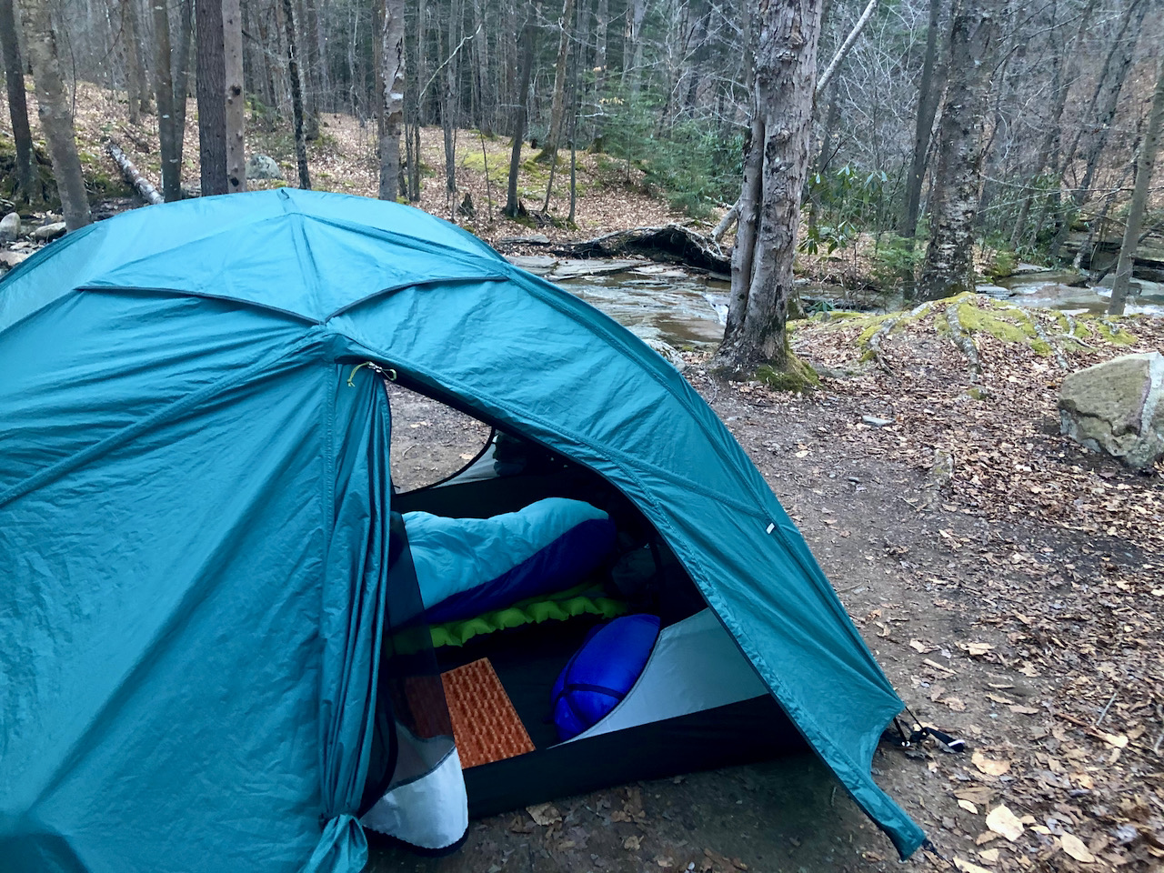 Photo of a setup tent with the door open placed in front of running water