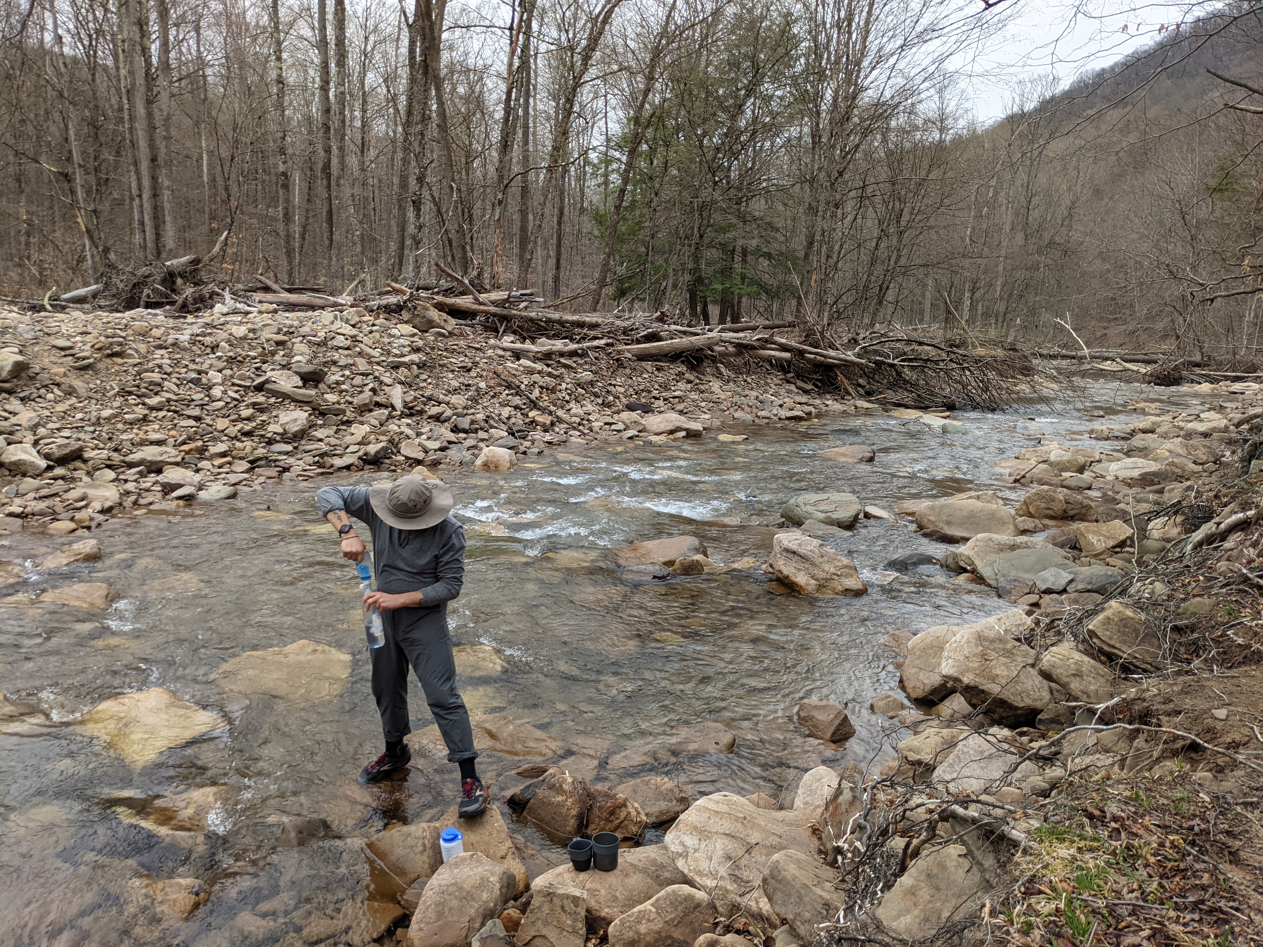 Photo of Brett standing in the stream filtering water into a bottle